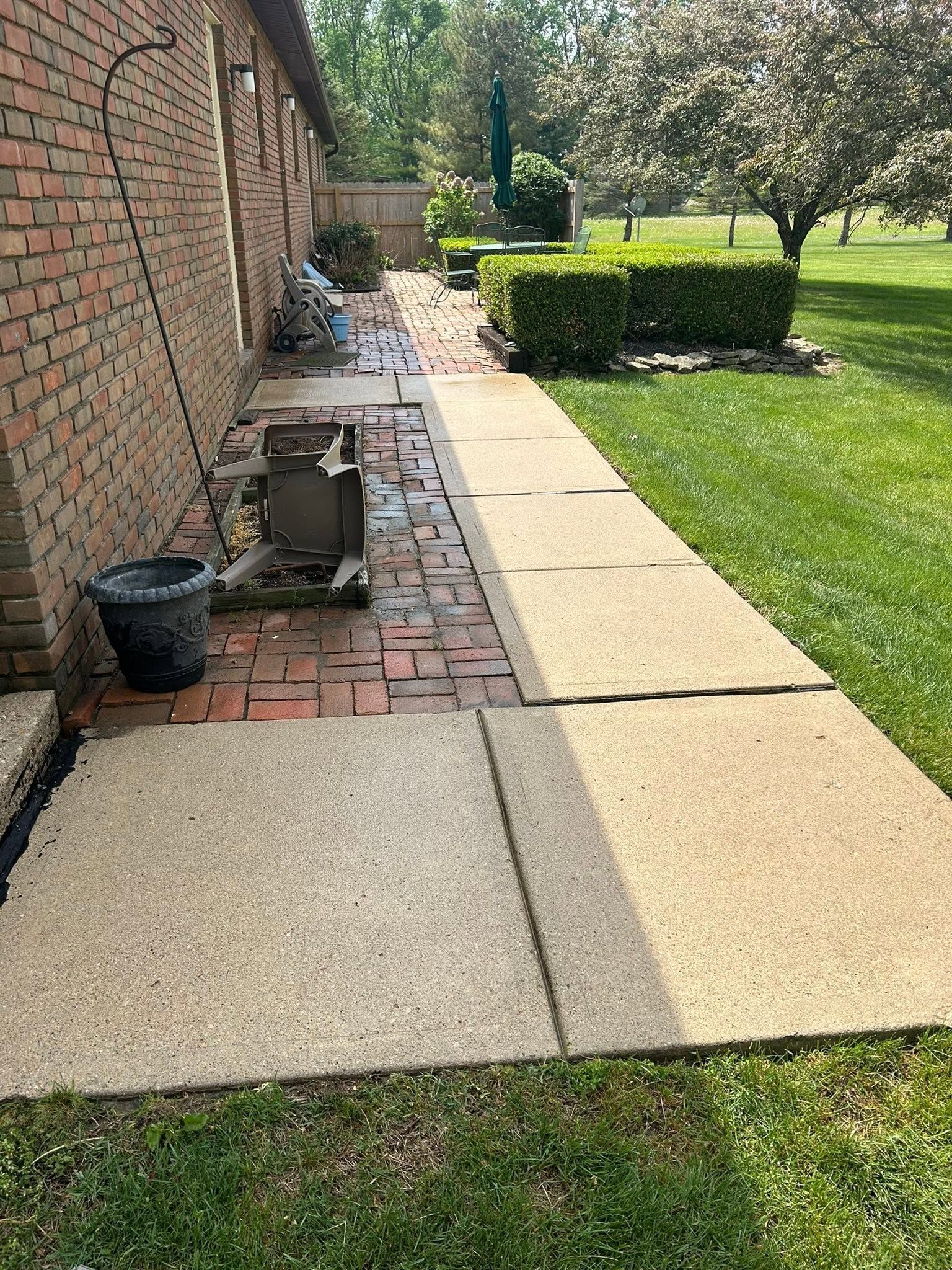 Brick side yard path beside a house with potted plants, grass, and hedges in sunlight