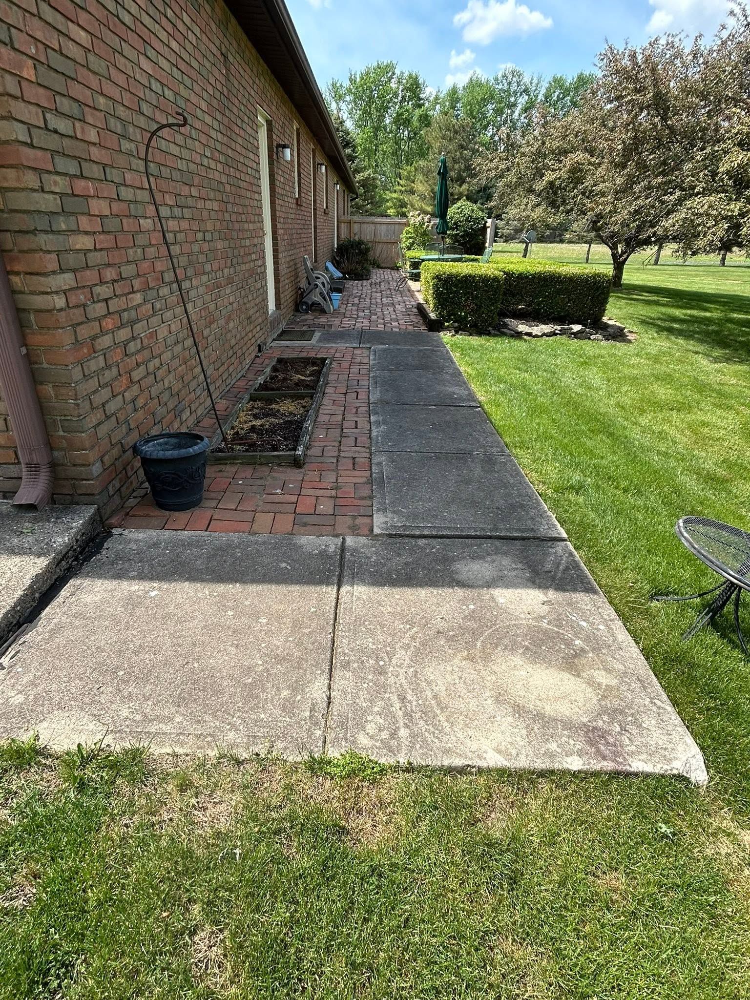 Brick house side yard with concrete walkway, grass lawn, and hedges on a sunny day