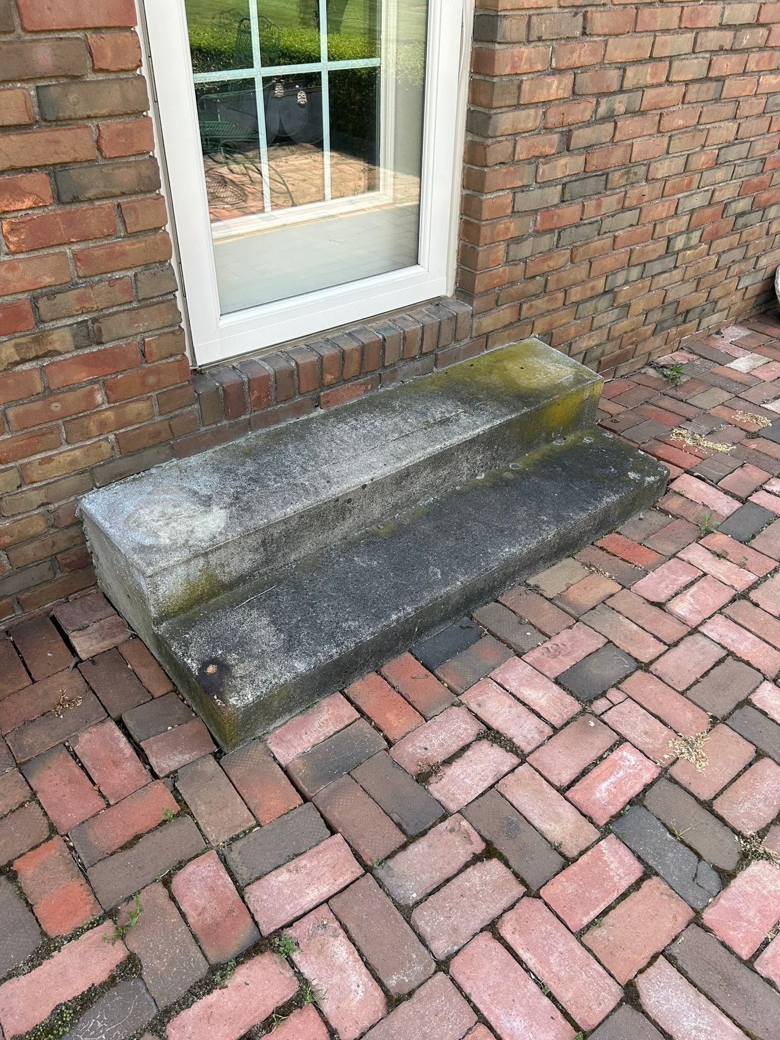Brick step with a yellow-stained stone landing beside a white-framed door on a brick patio.