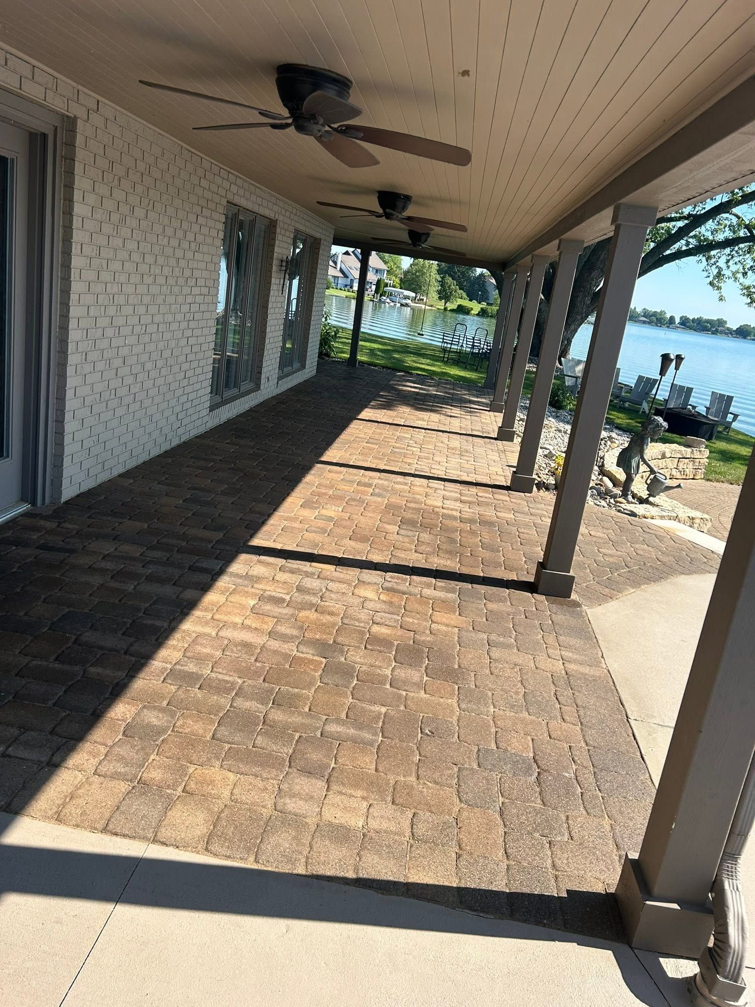 Covered patio with brick floor, ceiling fans, and water view beyond the pillars.
