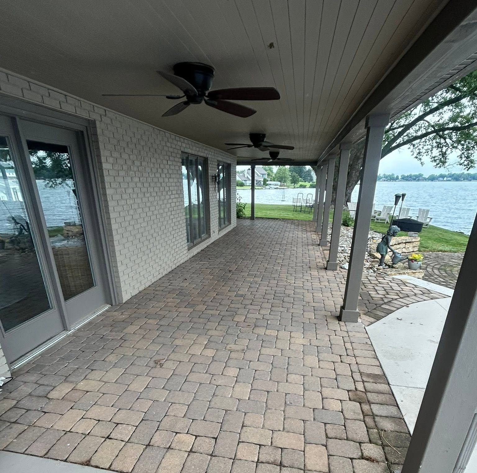 Covered stone patio with ceiling fans, sliding glass doors, and a lakeside view beyond the railing