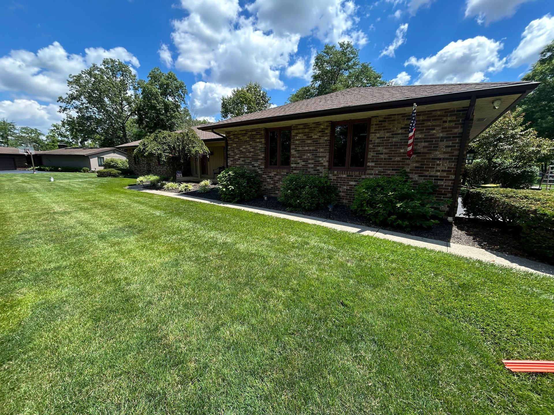 Single-story brick house with a shingled roof and a green lawn under a bright blue sky