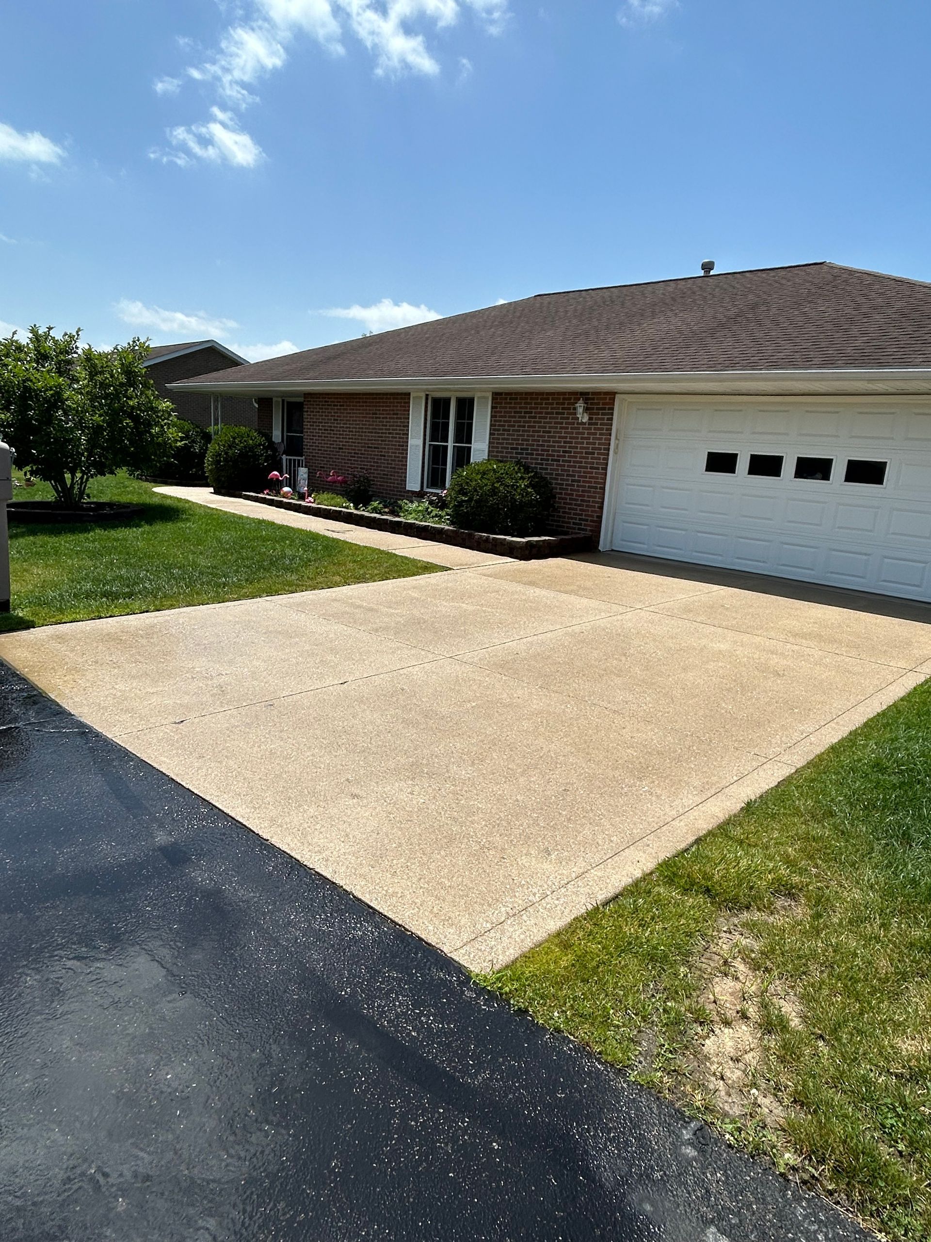 Suburban house with a tan driveway, white garage door, green lawn, and dark asphalt street.