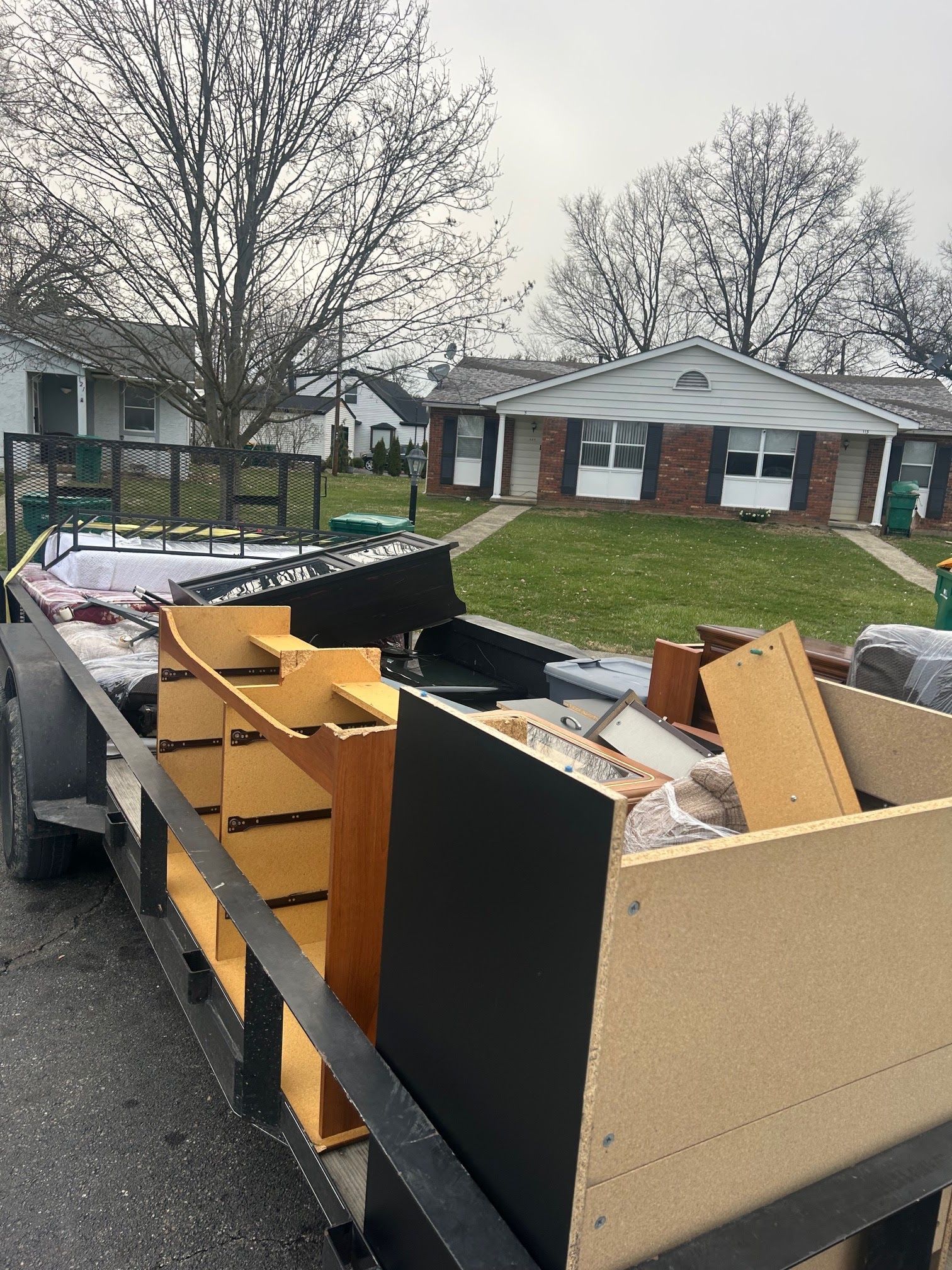 Trailer loaded with wooden furniture and boards in a residential driveway on a cloudy day