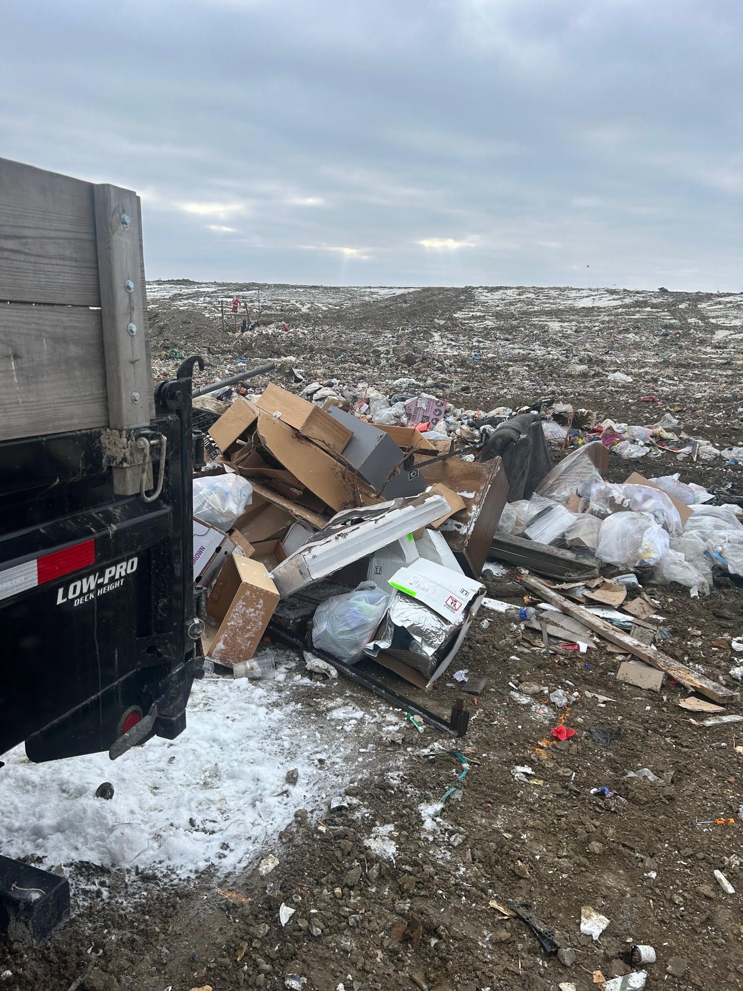 Overflowing roadside trash pile beside a black truck in a snowy, overcast dump area