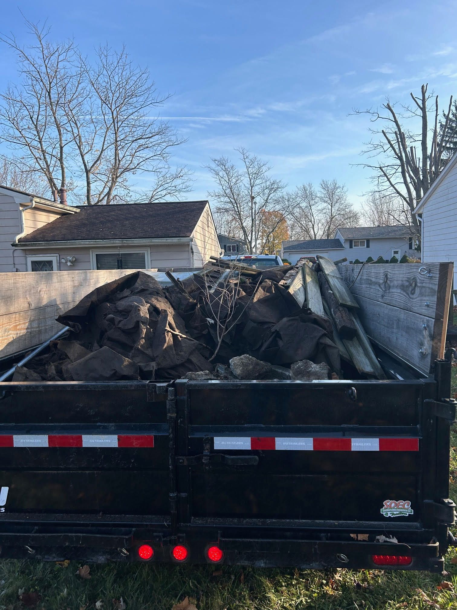 Black dump trailer filled with charred debris parked in a driveway under a blue sky.