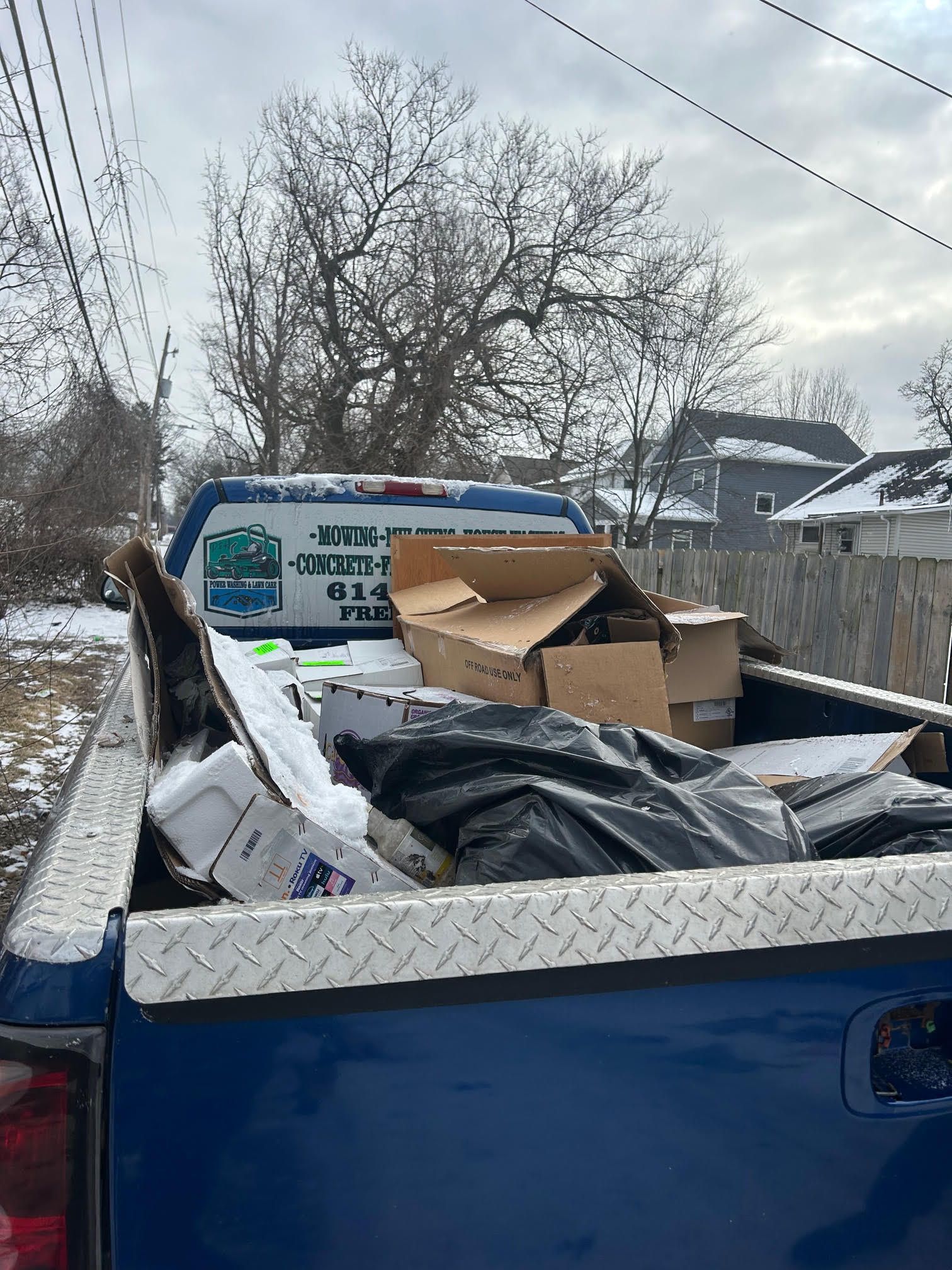 Blue pickup truck bed filled with cardboard boxes and trash in a snowy alley