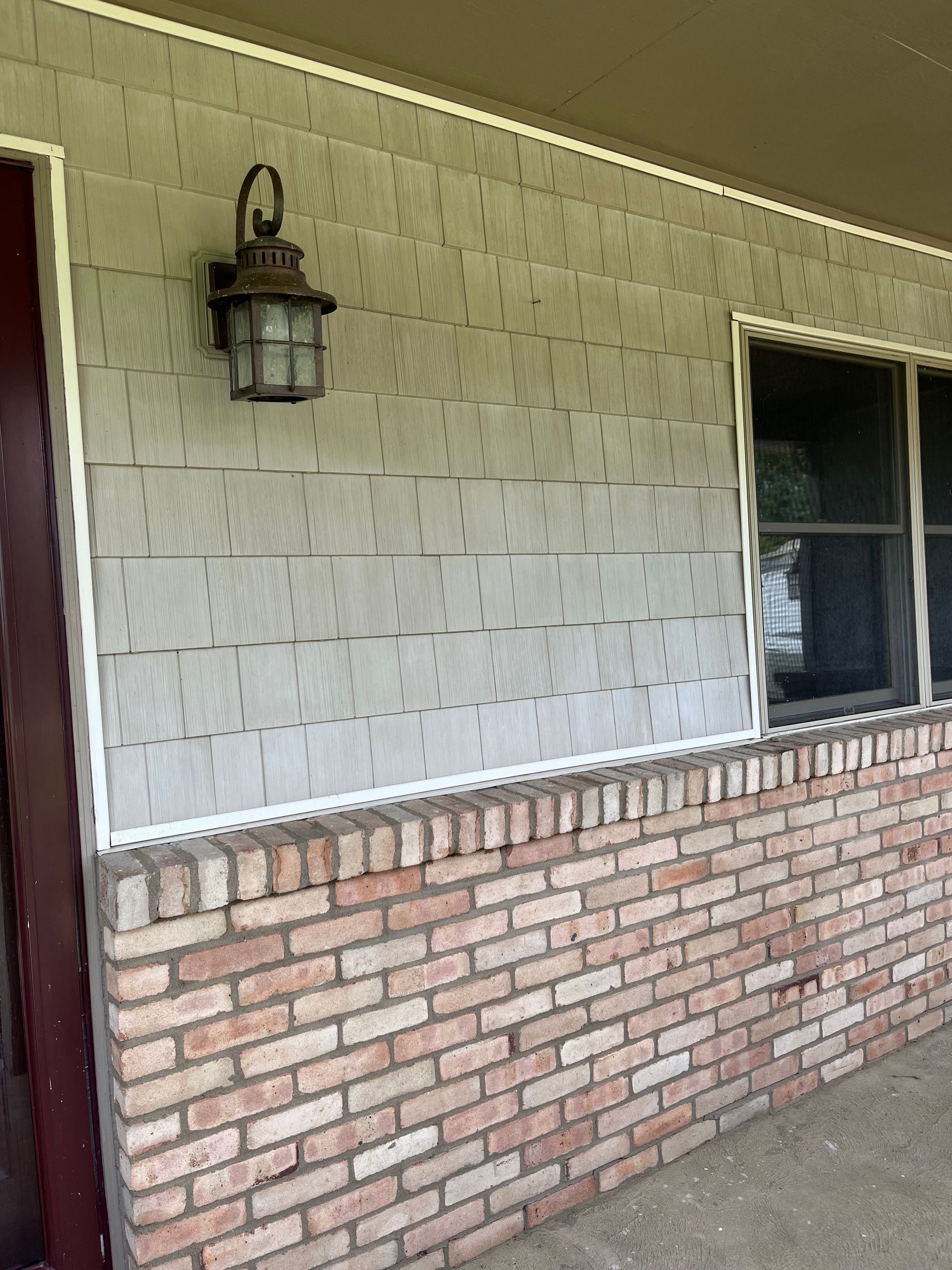 Covered porch with white brick wall, lantern light, and a screened window above a brick base.