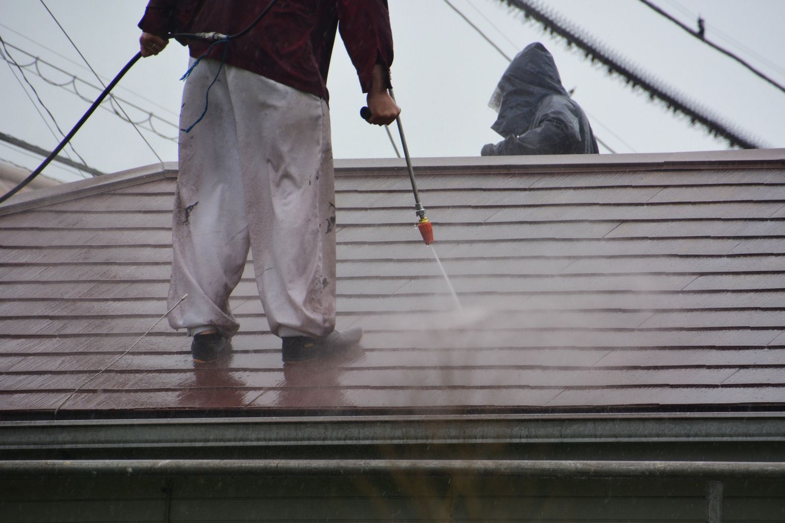 Workers power-washing a sloped roof on a rainy day