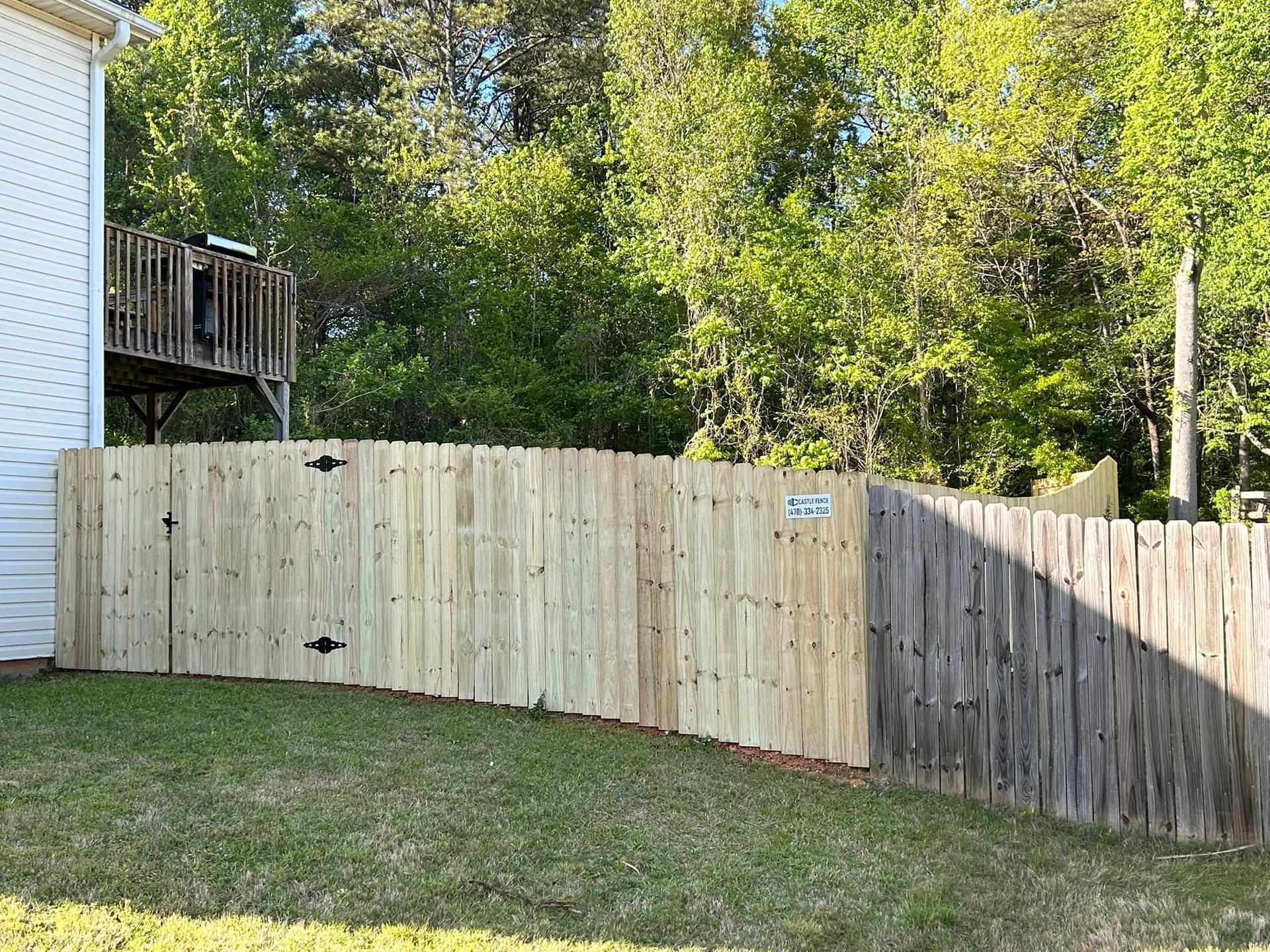 Backyard with a curved wooden fence, green lawn, trees, and part of a house deck on the left
