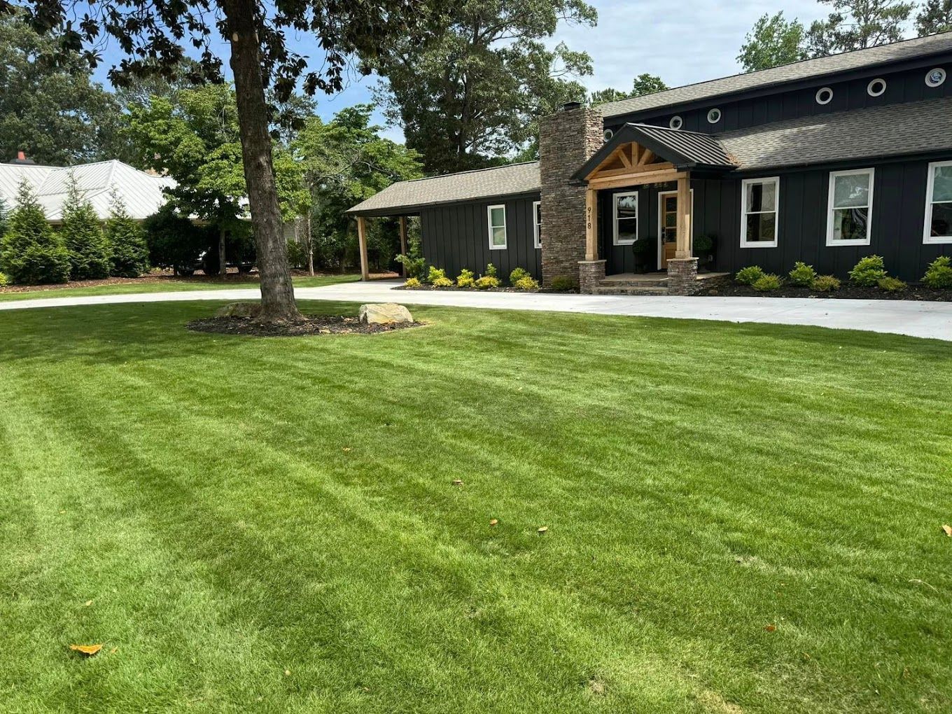 Lush green lawn in front of a dark building with a covered entrance and large trees.