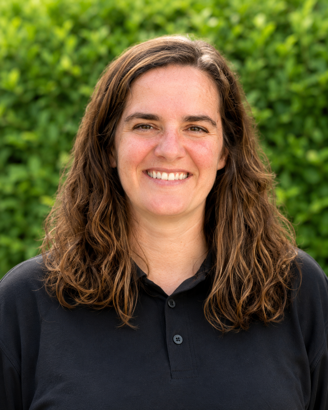 Ashton Price, Lead Copywriter & Content Strategist Portrait of a smiling person in a black polo shirt against a green leafy background