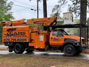 Orange utility truck with bucket lift parked on a wet roadside near trees and power lines