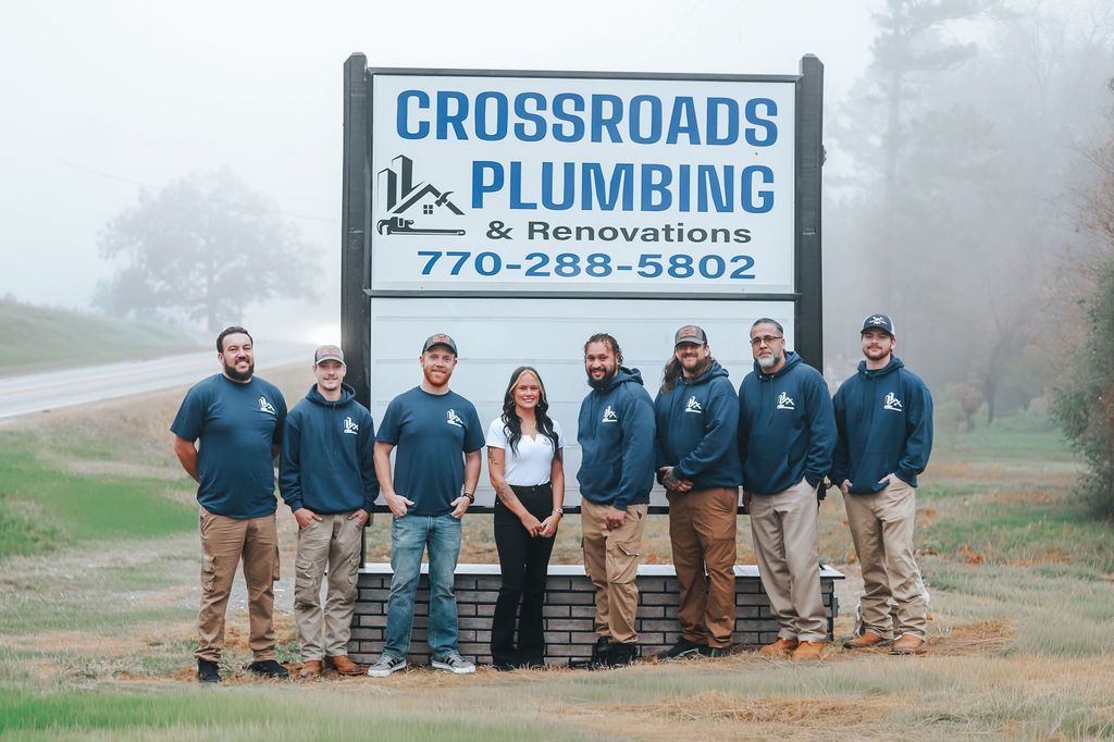 Crossroads Plumbing team standing in front of a company sign in a foggy outdoor setting