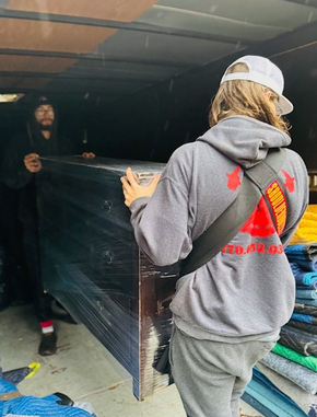 Two workers moving a wrapped black panel in a dim garage-like space