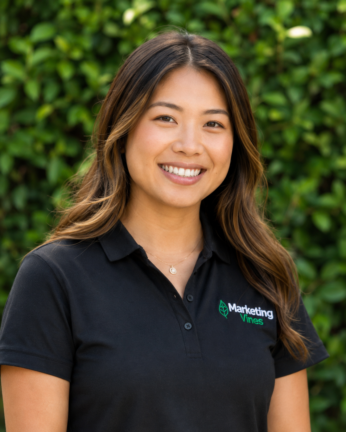 Lena Nguyen, Creative Director & Brand Designer for Home Service Businesses Smiling person in a black polo shirt with a marketing logo, standing outdoors against green foliage