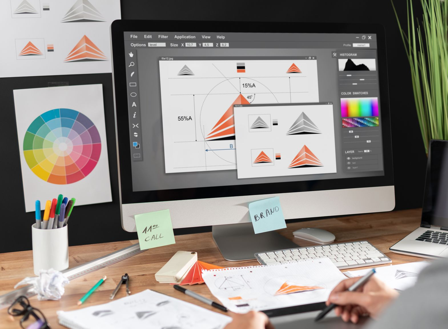 Designer working on a desktop computer with color palettes and sketches on a cluttered desk