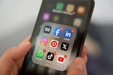 Hand holding a smartphone showing a social media folder with app icons on screen