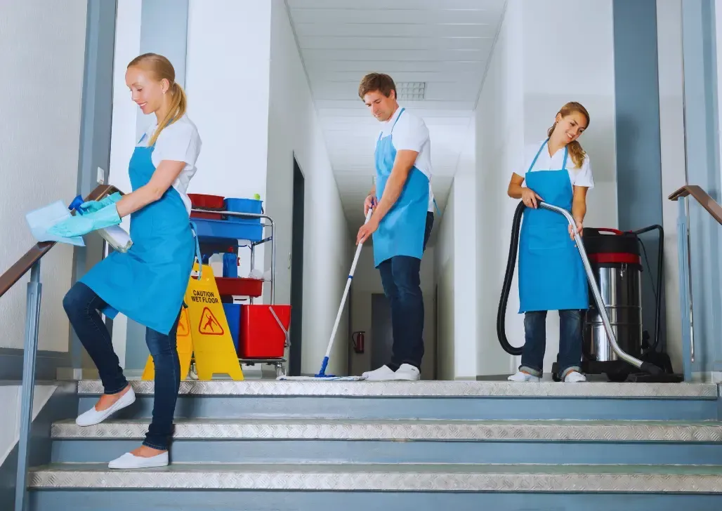 Office Cleaning Services Las Vegas-Three cleaning staff in blue aprons on stairs, one carrying supplies, one mopping, and one vacuuming.