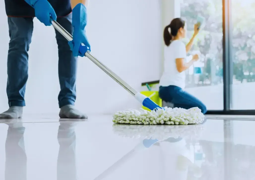 Office Cleaning Services Las Vegas-Two people clean a room, one mopping the shiny floor and the other wiping a large window.