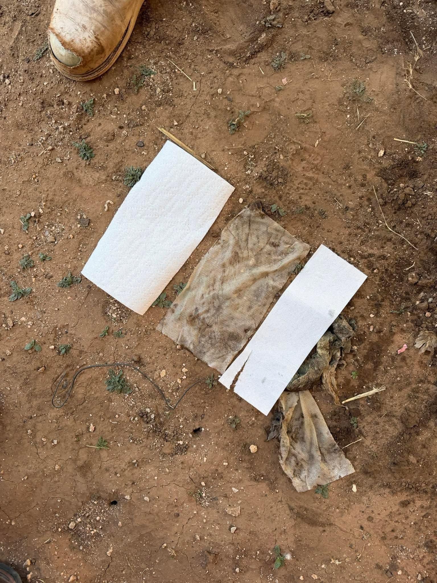 Open cardboard box on dirt ground with white foam pieces and a plastic bag nearby