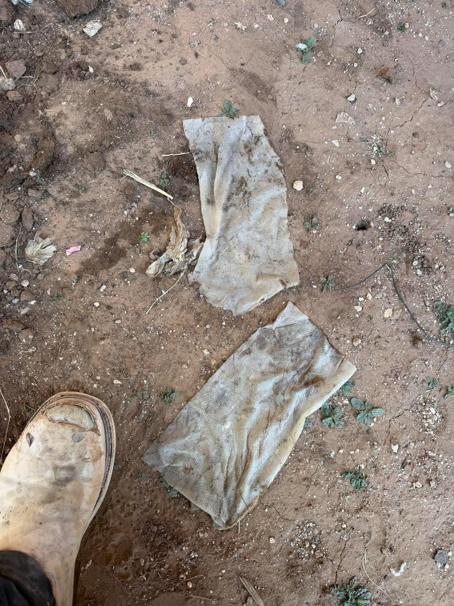 Two torn gray fabric pieces on dirt beside a tan boot.