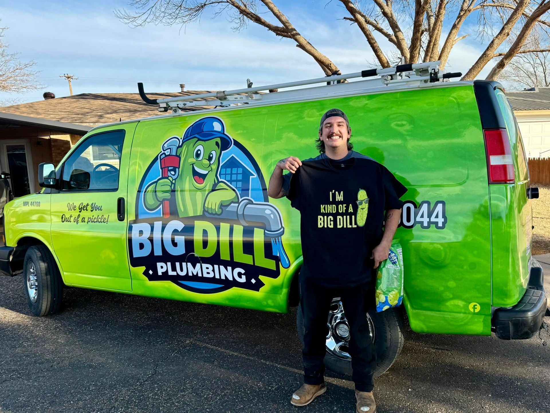 Person standing by a bright green Big Dill Plumbing van with cartoon pickle logo, holding up a drink outdoors.