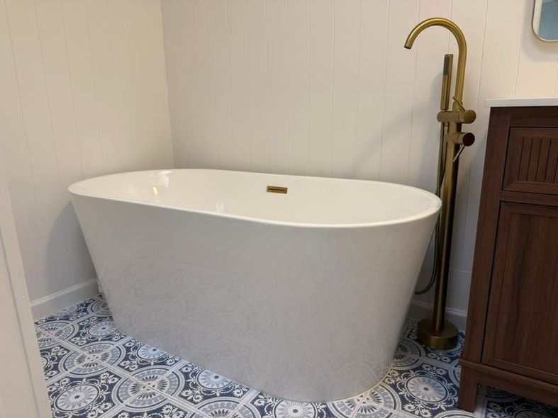 White freestanding bathtub with brass floor faucet in a bathroom with blue patterned tile floor