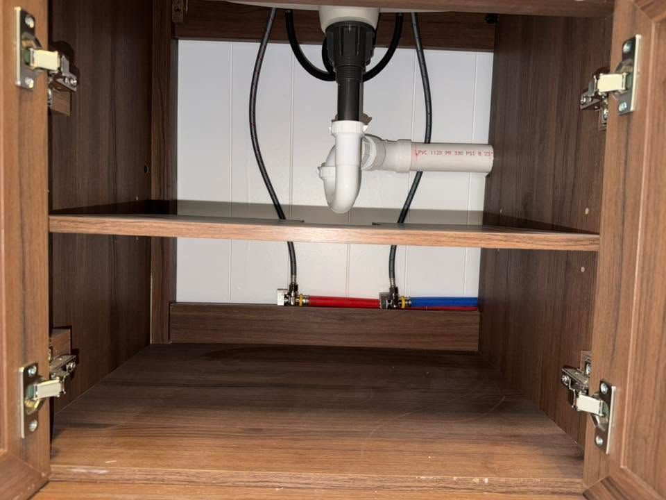 Under-sink cabinet with exposed plumbing and shutoff valves inside wooden doors