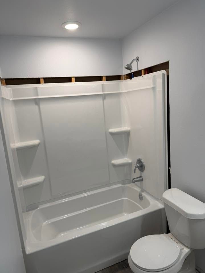 White bathroom with a shower-tub combo, built-in shelves, and a toilet under a sloped ceiling.