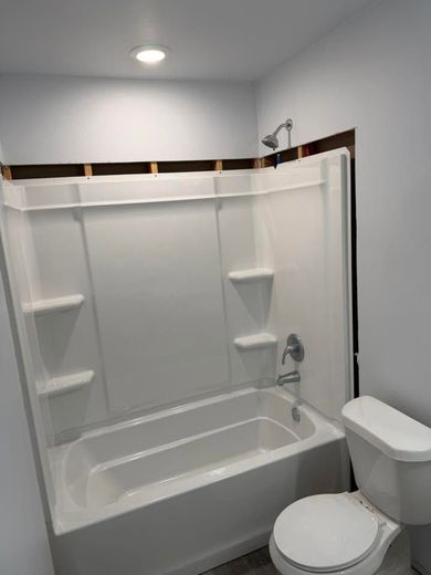 White bathroom with a shower-tub combo, built-in shelves, and a toilet under a sloped ceiling.