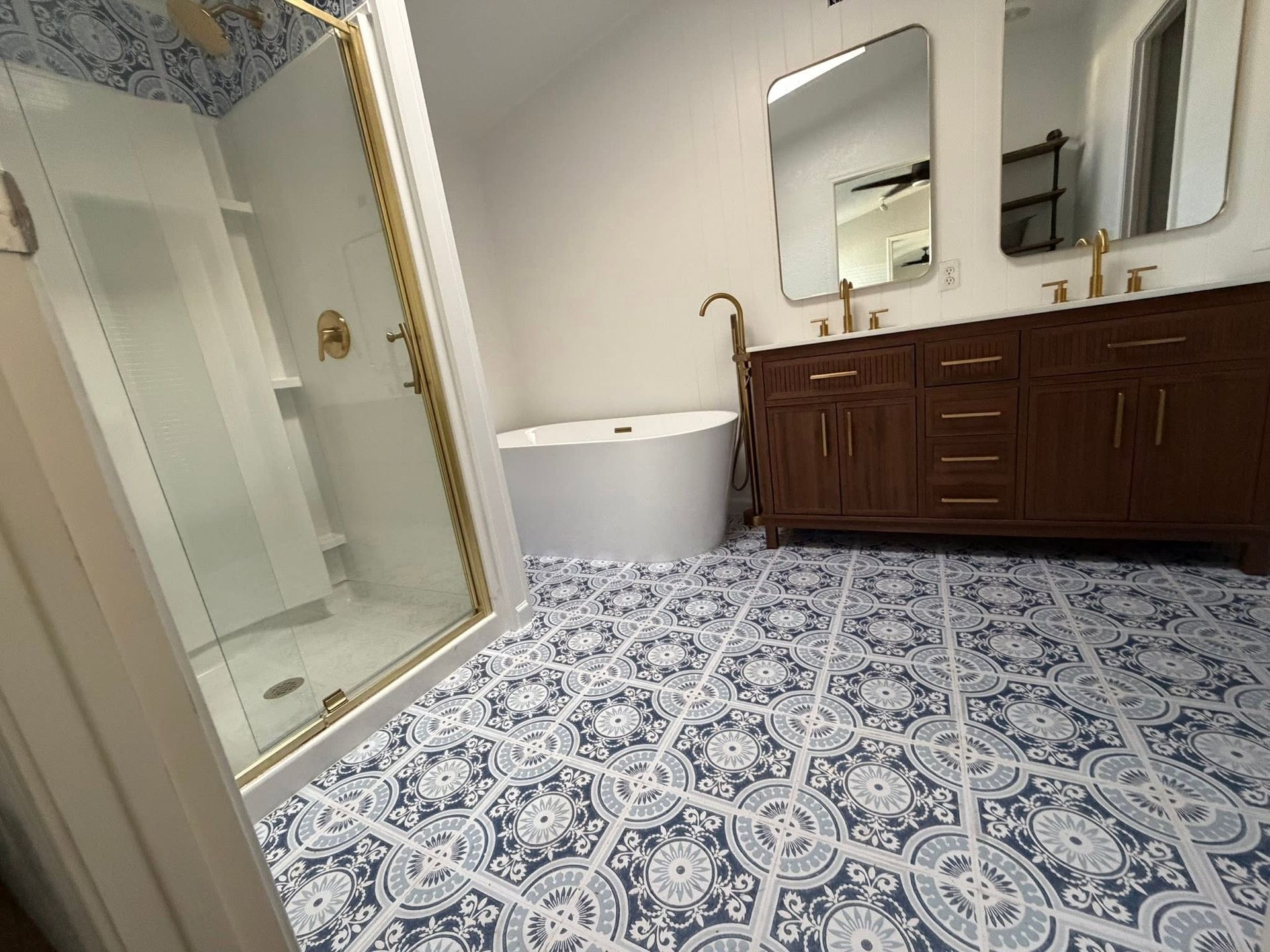 Bathroom with patterned blue tile floor, glass shower, white tub, and dark wood vanity with mirror cabinets