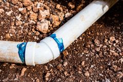 White PVC pipe elbow joint leaking under brown dirt, with blue sealant visible around the connection
