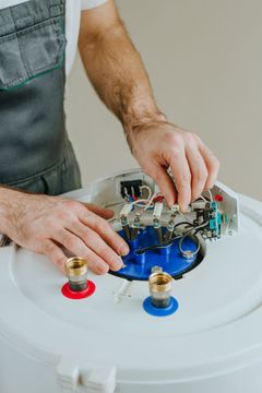 Hands repairing a white appliance with exposed blue interior and wires