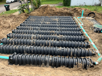 Installation of a septic drain field with multiple rows of black plastic chambers and green pipes, in a residential yard.