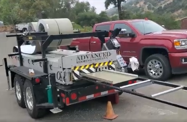 Roofing equipment trailer, silver and black, with red pickup truck in background.