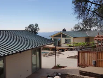 Two houses with green roofs on a sunny day. One has a patio and a pool area.