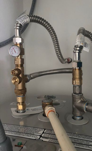 Blue-gloved hand near a garbage disposal under a sink. Water or liquid present.