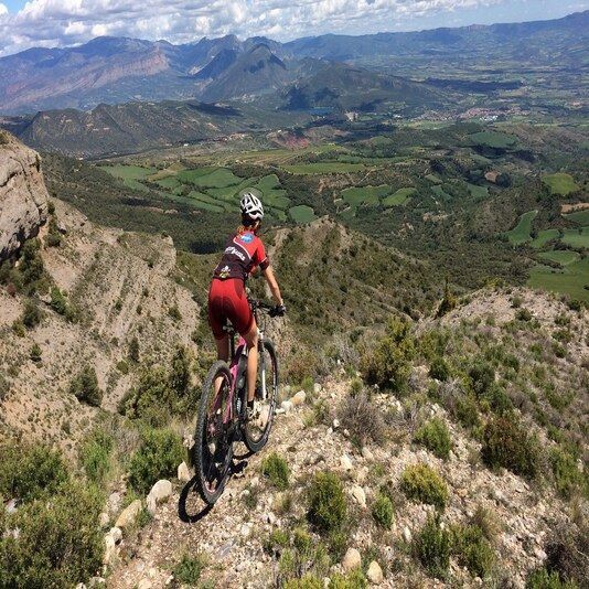 Una persona baixant amb bicicleta per un turó amb muntanyes al fons