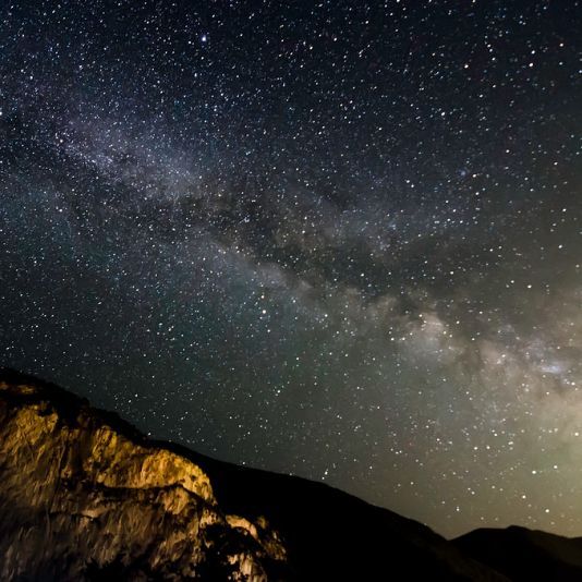 Un cel nocturn ple d'estrelles i muntanyes en primer pla.