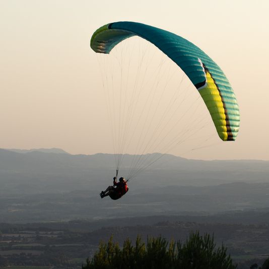 Una persona fa parasailing sobre una vall amb muntanyes al fons