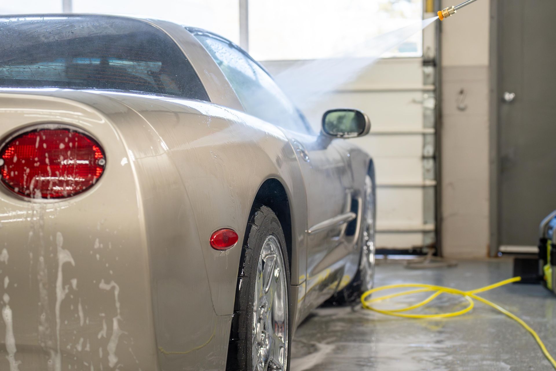 A car is being washed with a hose in a garage.
