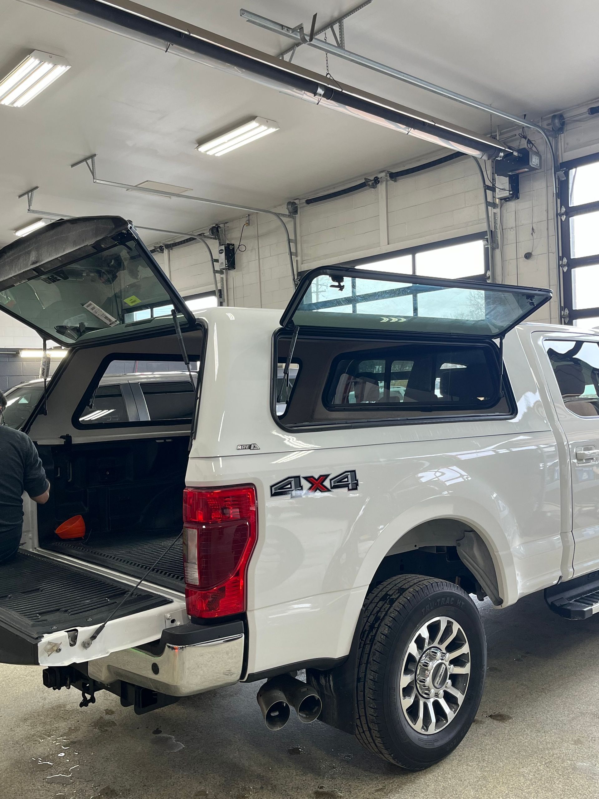 A white truck with the bed open is parked in a garage.