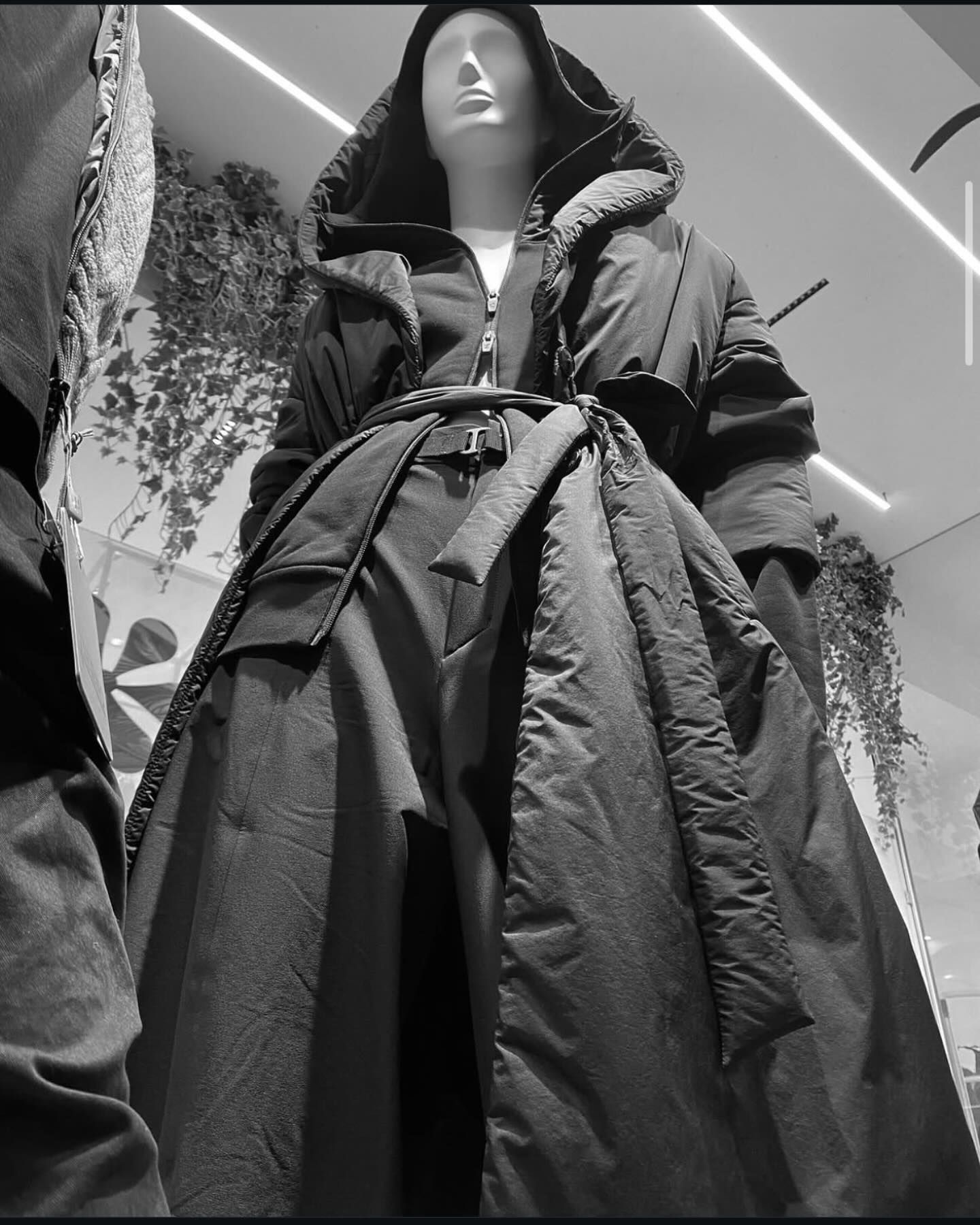 Espositore di abbigliamento nero in un negozio. Un completo felpa e gonna su un manichino. Altre felpe su un'asta e una borsa tote.