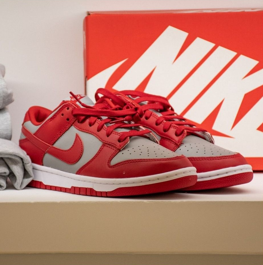 Scarpe da ginnastica Nike Dunk Low rosse e grigie con scatola su uno scaffale.