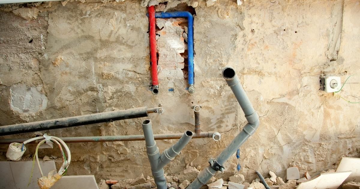 Plumbing pipes exposed in a wall during renovation; red and blue pipes with a gray sewage pipe.