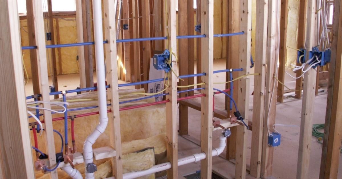 Interior construction: Wooden framing with blue, red, and white pipes, electrical wiring, and blue electrical boxes.