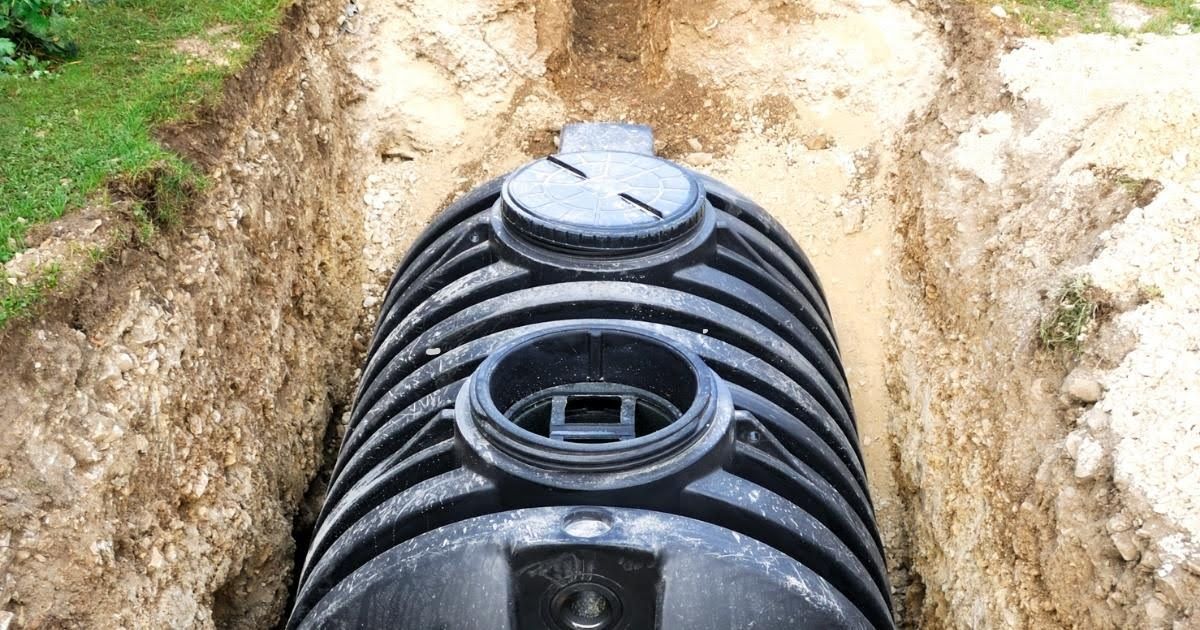 A large black septic tank is sitting in the dirt in a trench.