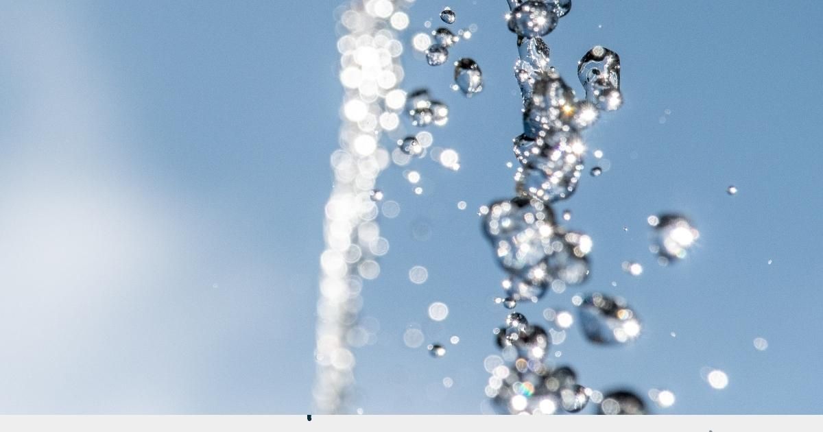 Water droplets splashing upward against a clear blue sky.