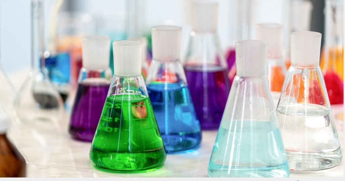 Assorted colorful liquid-filled lab flasks on a white table in a laboratory setting